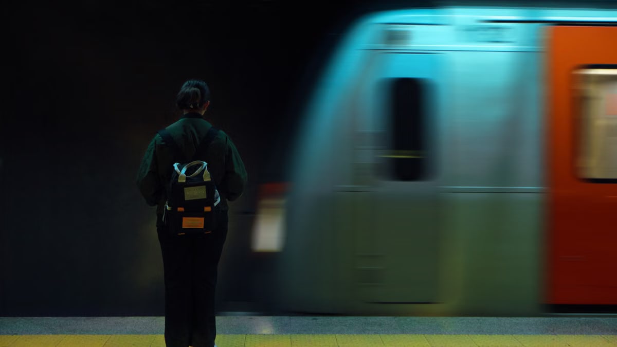 A woman with a backpack stands at an Ankara metro station as a train speeds by.